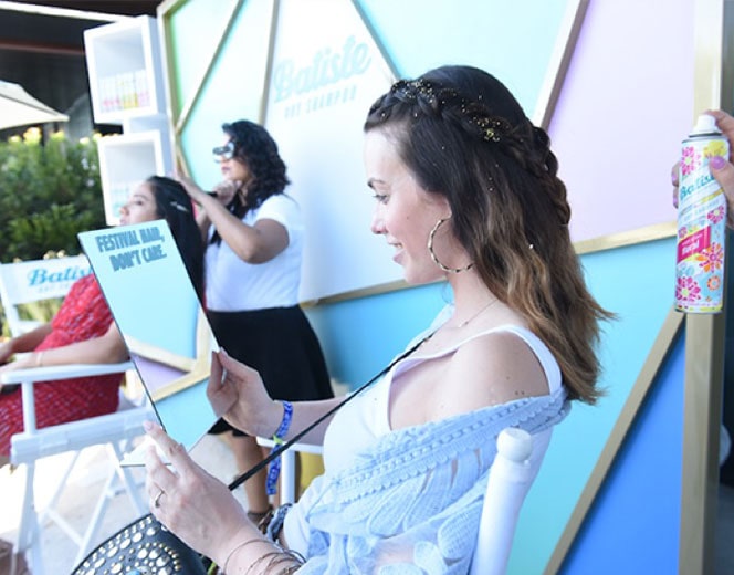 Woman checking out her hair in a mirror after having a hair refresh at the Batiste Dry Shampoo braid bar, a marketing initiative created by the HUNTER integrated marketing and PR firm in NYC, and held at the Coachella music festival.